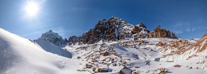Snow-covered rocky mountains under a bright blue sky in Almaty, showcasing the region's stunning winter landscapes and natural beauty.
