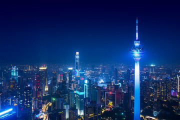 A vibrant night view of the Kuala Lumpur skyline featuring the illuminated Kuala Lumpur Tower. The tower stands tall among the cityscape, surrounded by modern skyscrapers and a network of lit highways, symbolizing the dynamic and urban charm of Malaysia's capital