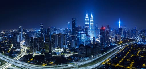 This image showcases a stunning night view of Kuala Lumpur, Malaysia, featuring the iconic Petronas Twin Towers illuminated against the city skyline. The dazzling highways and vibrant cityscape highlight the modern attractions of Malaysia.