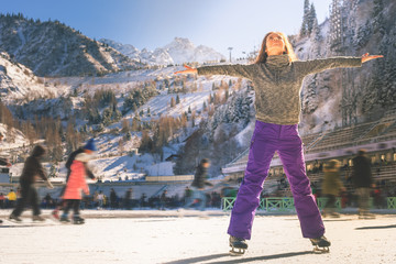 A girl gracefully skating with arms outstretched surrounded by a snowy mountain backdrop and other skaters enjoying the ice. Keywords: