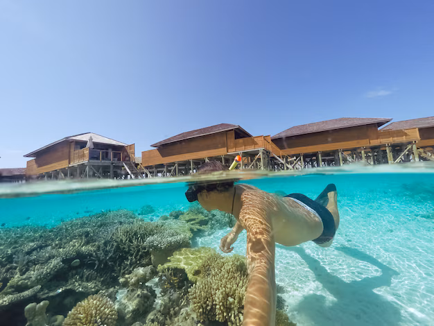 A man swimming in the turquoise waters of the beach with the luxurious Centara Ras Fushi Resort Maldives overwater villas in the background