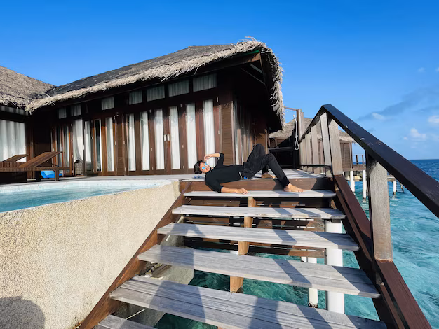 Centara Ras Fushi Resort Maldives: A man enjoying a peaceful moment on a wooden jetty surrounded by crystal-clear turquoise waters and a stunning Maldivian backdrop.